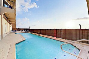 A swimming pool with a sunshade, lounge chairs, and a fence. - Florence II Condominiums #201 (South Padre Island)