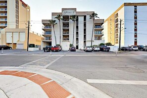 A multi-story hotel with a central entrance, parking lot, and palm trees. - Florence II Condominiums #201 (South Padre Island)