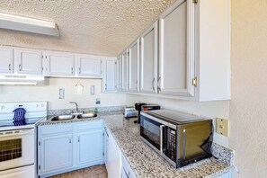 A kitchen with white cabinets, a stove, a microwave, and a toaster. - Florence II Condominiums #201 (South Padre Island)