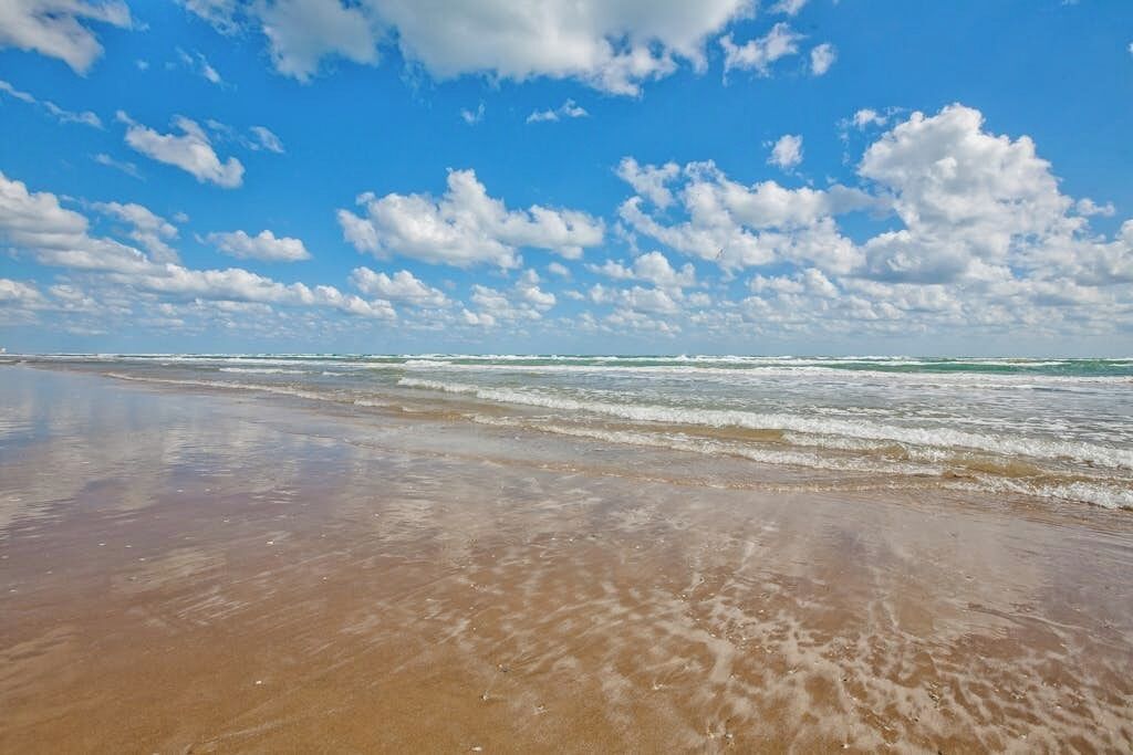 A beach with waves, clear sky, and clouds.