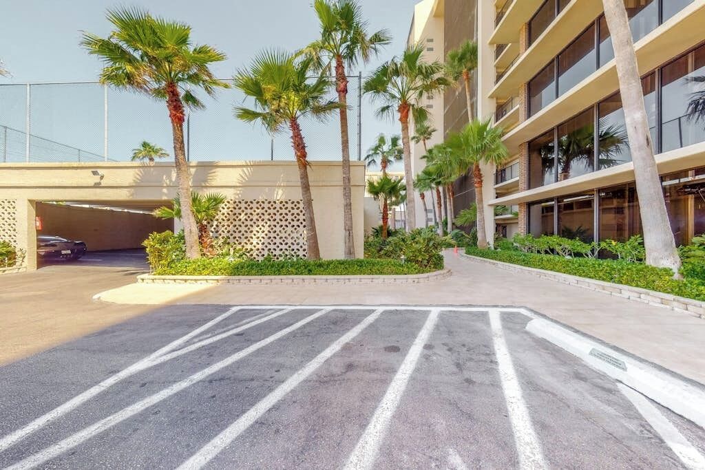 A parking lot with marked parking spaces, a building with multiple floors, and palm trees.