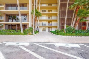 A multi-story hotel with a central courtyard, palm trees, and a parking area with marked spaces. - Ocean Vista Condominiums #102 (South Padre Island)