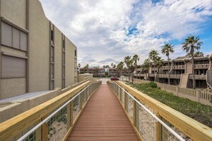 A wooden boardwalk leading to a building with multiple balconies, surrounded by palm trees. - Beachview Condominiums #204 (South Padre Island)
