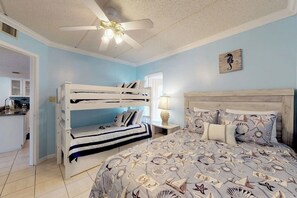 A bedroom with bunk beds, a bed with a nautical-themed bedspread, a ceiling fan, and a seahorse wall art piece. - Beachview Condominiums #204 (South Padre Island)