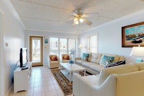 A living room with a ceiling fan, a television, a sofa, a coffee table, and a painting on the wall. - Beachview Condominiums #204 (South Padre Island)