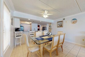 A dining area with a glass table, white chairs, and a ceiling fan. - Beachview Condominiums #204 (South Padre Island)