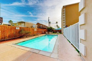 A swimming pool with a wooden fence, a concrete walkway, and a building with a balcony. - Escape Condominiums #7 (South Padre Island)