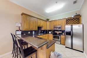 A kitchen with wooden cabinets, a stainless steel refrigerator, and a granite countertop. - Escape Condominiums #7 (South Padre Island)