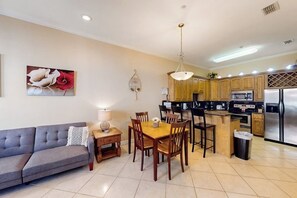 A modern kitchen with wooden cabinets, a dining area with a table and chairs, and a gray sofa. - Escape Condominiums #7 (South Padre Island)