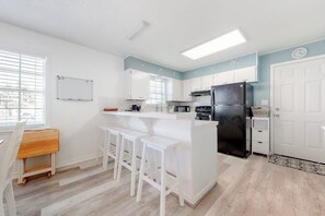 A modern kitchen with white cabinetry, a black refrigerator, and a bar area with white stools. - Lazy Seagull Beach House (South Padre Island)