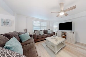 A living room with a sofa, a coffee table, a television, and a ceiling fan. - Lazy Seagull Beach House (South Padre Island)