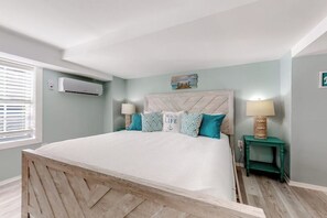 Een slaapkamer met een groot bed, een hoofdbord met een herringbone-patroon, twee bedlampjes en een kleine tafel met een lamp.