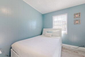 A bedroom with a bed, a window with blinds, and two wall-mounted picture frames. - Lazy Seagull Beach House (South Padre Island)