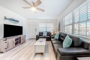 Ein modernes Wohnzimmer mit Flachbildfernseher, Deckenventilator, Sofa und Couchtisch.