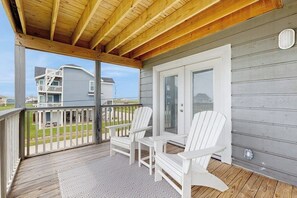 A covered porch with two Adirondack chairs, a patterned rug, and a view of a two-story building. - Seabreeze Serenity - Beachfront & Dog-Friendly (Galveston)