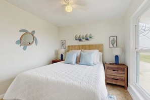 A bedroom with a large bed, a wooden headboard, a nightstand, and wall art. - Seabreeze Serenity - Beachfront & Dog-Friendly (Galveston)