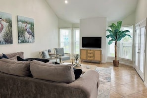 A living room with a sofa, a television, a cabinet, and a large plant. - Seabreeze Serenity - Beachfront & Dog-Friendly (Galveston)