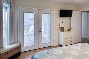 A bedroom with a bed, a dresser, a television, and a sliding glass door. - Seabreeze Serenity - Beachfront & Dog-Friendly (Galveston)