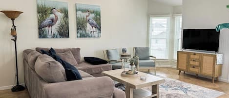 A living room with a sofa, armchairs, a coffee table, a TV, and artwork on the wall.