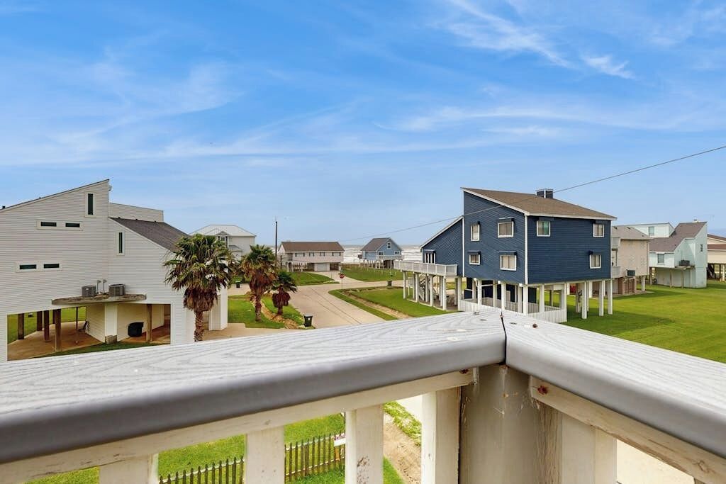 A residential neighborhood with houses, a clear sky, and a balcony with a railing.
