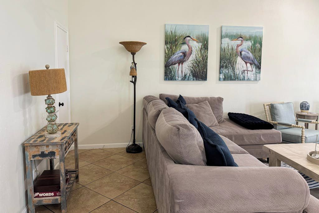 En stue med en beige sofa, en lampe, et sofabord med en pynteting, og to billeder af en fugl hængt på væggen.