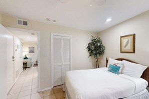 A bedroom with a bed, a door, a plant, and a framed picture on the wall. - La Internacional Condominiums #210 (South Padre Island)