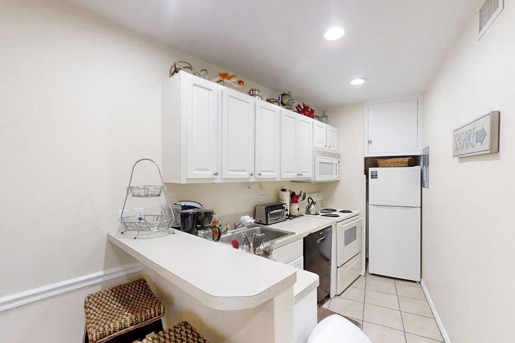 Una cocina compacta con armarios blancos, horno integrado y refrigerador.