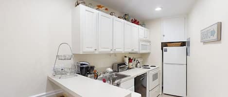 Una cocina compacta con armarios blancos, horno integrado y refrigerador.