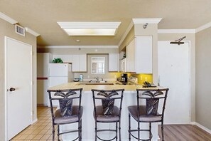 A kitchen with a central island, three chairs, and a refrigerator. - San Luis Paradise #930 (Galveston)
