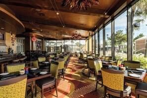 A restaurant with multiple tables and chairs, large windows, and a ceiling with hanging lights. - San Luis Paradise #930 (Galveston)