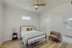Ein Schlafzimmer mit einem Bett, Nachttischen, einem Sessel, einem Kleiderschrank und einem Deckenventilator.