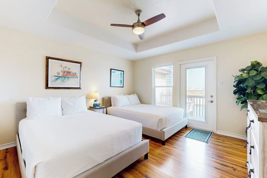 A hotel room with two beds, a ceiling fan, a door leading to a balcony, and a framed picture on the wall.