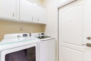 A laundry room with two washing machines and a dryer, a white door, and white cabinetry. - Cabana Cove - Channel-Front, Game Room & Kayaks (Corpus Christi)
