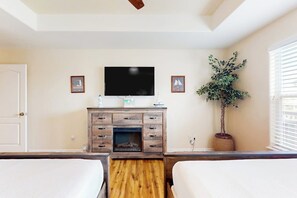 A hotel room with a wooden floor, a flat-screen TV mounted on the wall, a potted plant, and two beds. - Cabana Cove - Channel-Front, Game Room & Kayaks (Corpus Christi)