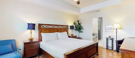 A bedroom with a wooden bed, a ceiling fan, a nightstand with a lamp, a blue chair, and a small table with a lamp.