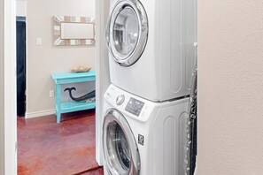 A laundry room with stacked washing machines, a blue bench, and a mirror on the wall. - Nemo Cay - Too The Beach (Corpus Christi)