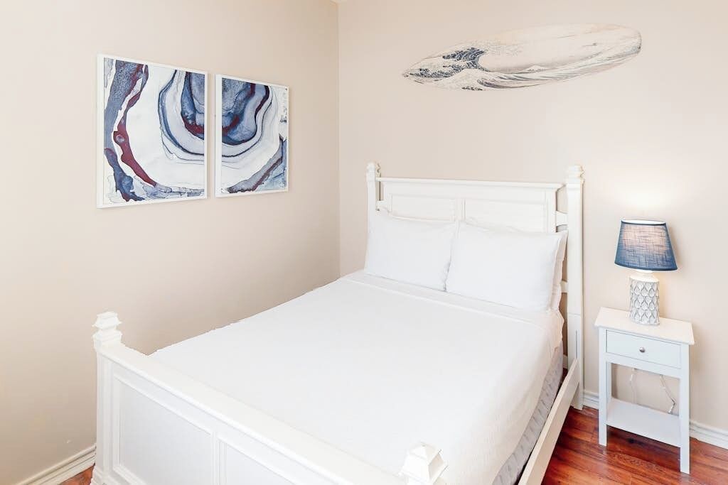 Ein Schlafzimmer mit einem weißen Bett, einem Nachttisch mit Lampe und abstrakter Kunst an der Wand.