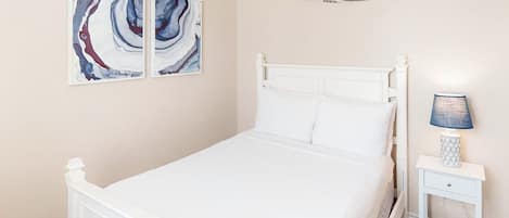 Ein Schlafzimmer mit einem weißen Bett, einem Nachttisch mit Lampe und abstrakter Kunst an der Wand.