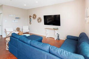 A living room with a sectional sofa, a television, decorative wall art, and a small table. - Nemo Cay - Too The Beach (Corpus Christi)