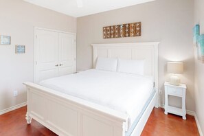 Un dormitorio con una cama grande, una mesita de noche blanca con lámpara y una puerta.