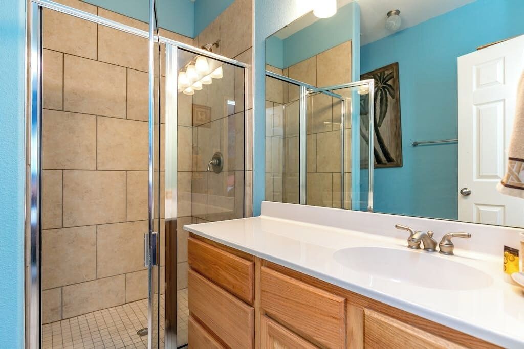A bathroom with a glass shower enclosure, a white sink, and wooden cabinetry.