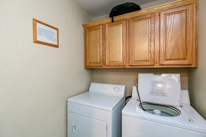 A laundry room with wooden cabinets above a washing machine and dryer. - NPI Hideaway Stay - Shared Pool, Near the Beach (Corpus Christi)