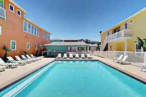 Une piscine avec des chaises longues, un bâtiment doté d’un toit végétalisé et un bâtiment jaune avec un balcon.