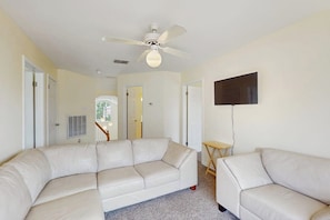 A living room with a white leather sofa, a small wooden table, and a ceiling fan. - Pelican Pete - Fireplace & Private Yard (Corpus Christi)