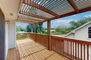 A wooden deck with a railing, a pergola overhead, and a view of a house and greenery. - Pelican Pete - Fireplace & Private Yard (Corpus Christi)