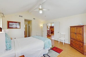 Une chambre avec deux lits, un ventilateur de plafond, une armoire en bois et un tableau encadré au mur.