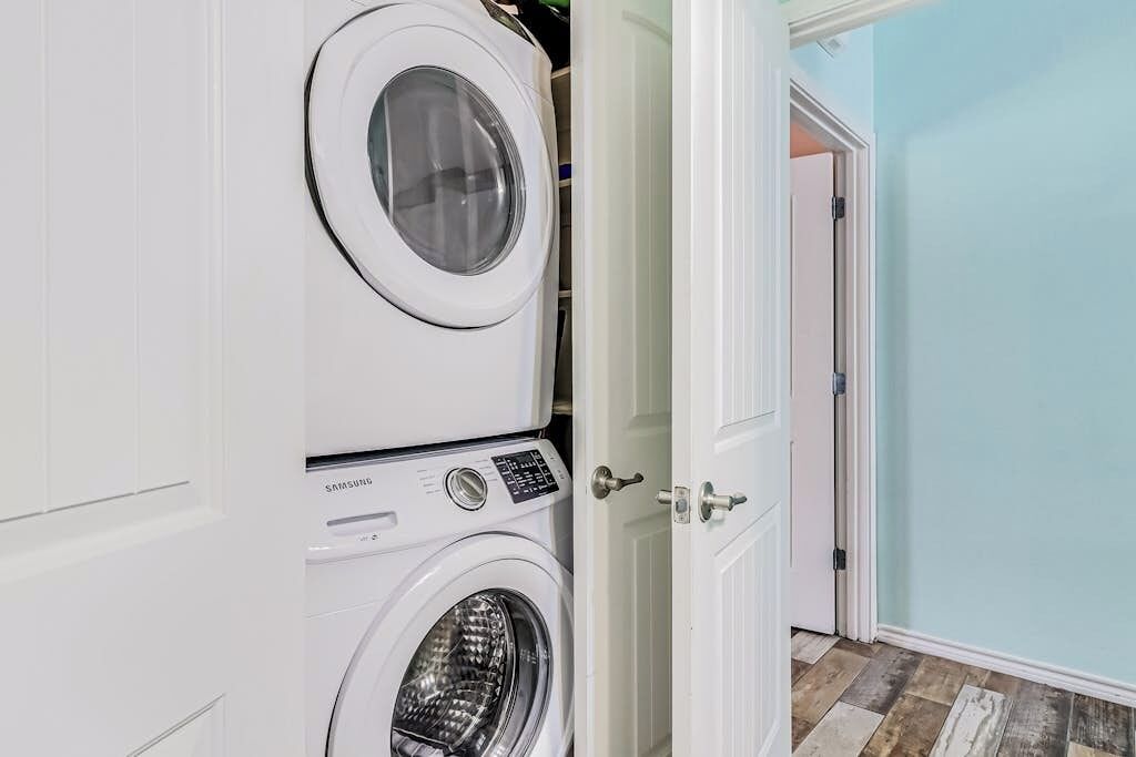 A laundry room with stacked washing machines and a door leading to another room.
