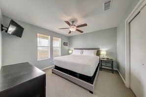 Ein Schlafzimmer mit einem Bett, einem Deckenventilator, einem an der Wand montierten Fernseher und einem Nachttisch mit einer Lampe.