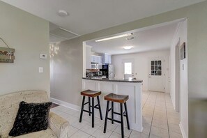 A modern kitchen with white cabinets, a central island, and two bar stools. - Wharf Cottage - Near Beach & Town, Dogs OK (Rockport)
