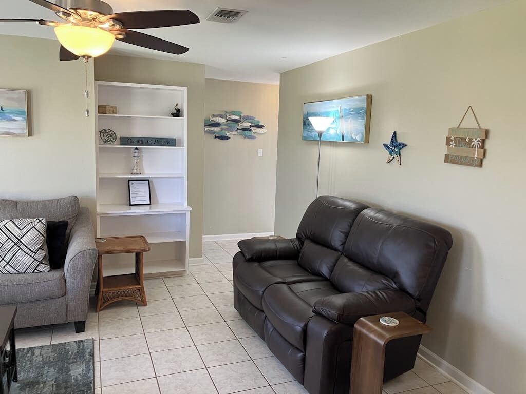 A living room with a ceiling fan, a sofa, a coffee table, a bookshelf, and wall art.